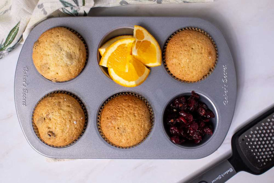 Cranberry orange muffins in a non-stick muffin pan with orange slices