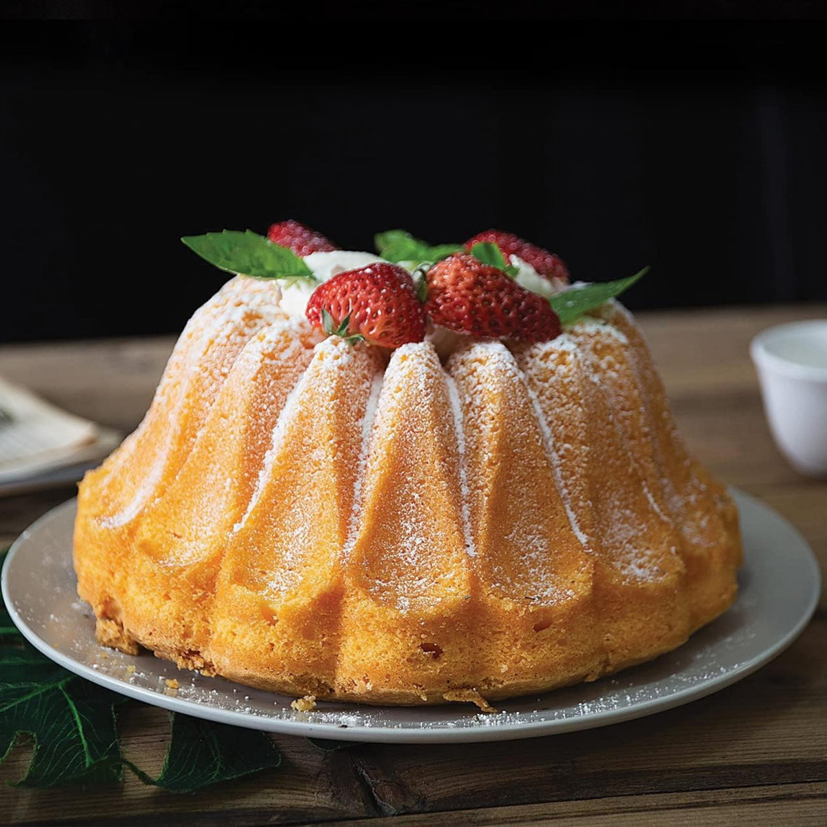 Vanilla fluted cake with powdered sugar and strawberries on a cake stand