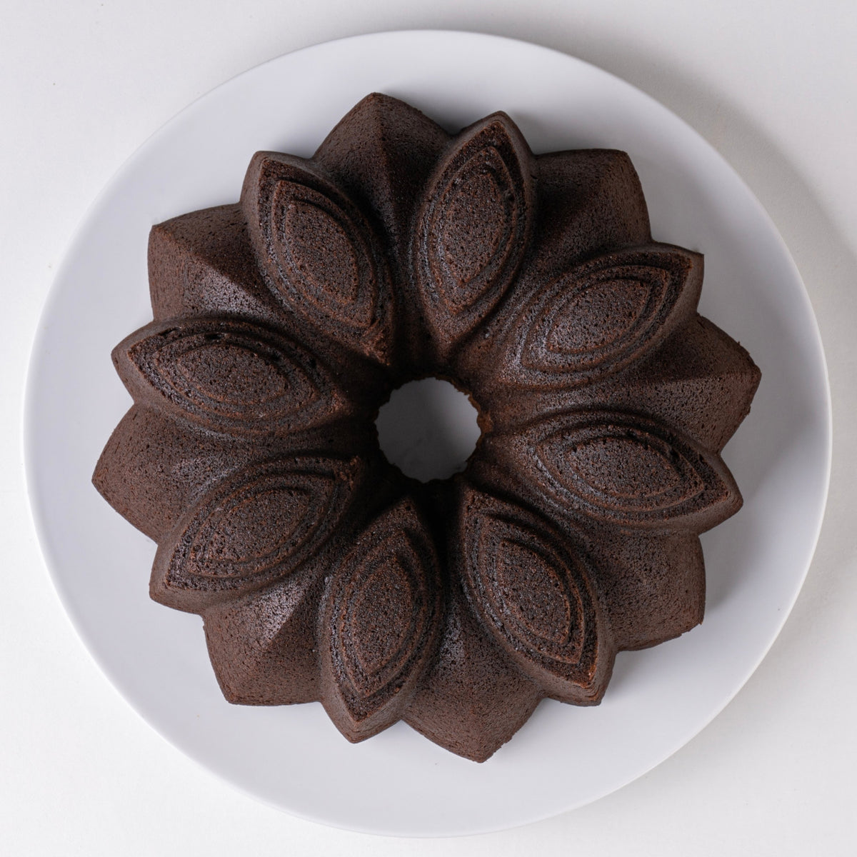 Chocolate flower-shaped fluted cake on a white plate, top view