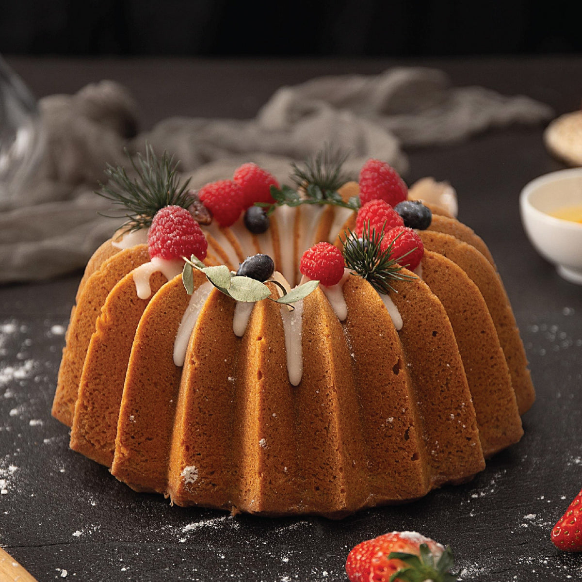 Golden wreath-shaped cake topped with berries on a dark table