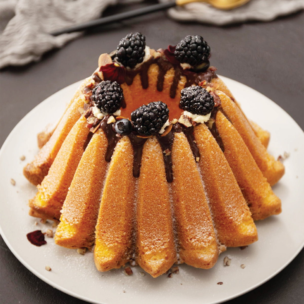 Fluted cake topped with whipped cream and blackberries on a white plate