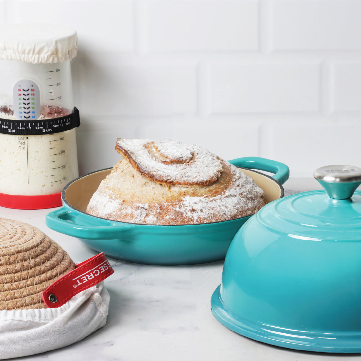 Sourdough starter jar beside a baked loaf in a teal Dutch oven