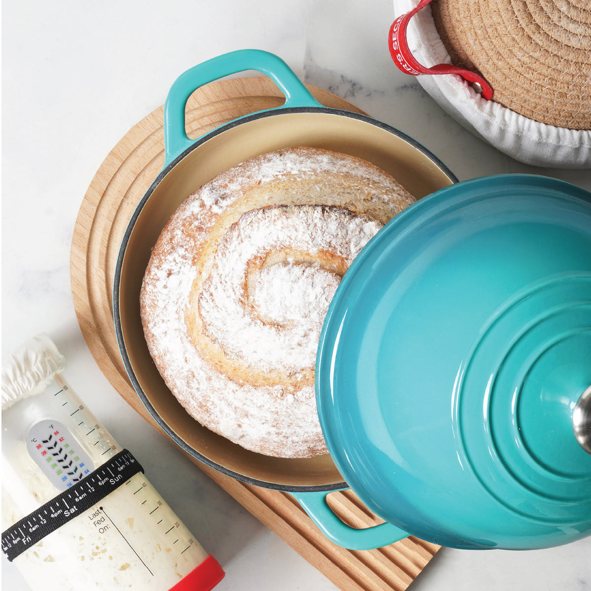 Sourdough loaf in a teal Dutch oven next to the starter jar