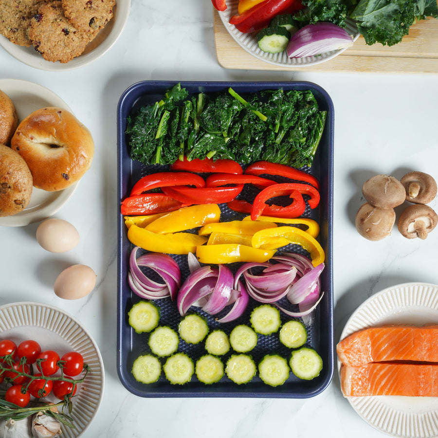 Bagels, peppers, onions and cucumber arranged on a sheet pan