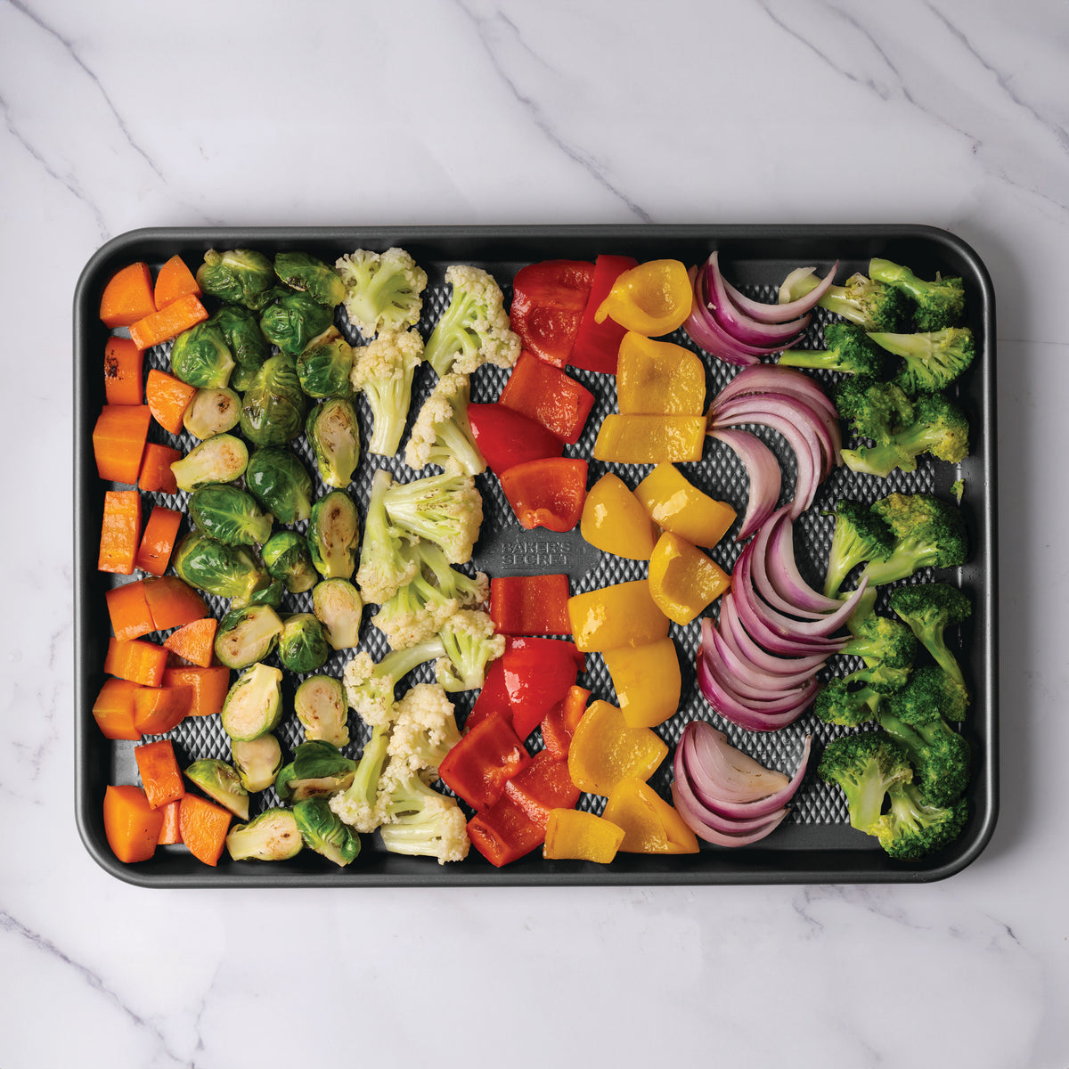 Colorful vegetables ready to roast on a dark diamond-texture sheet pan