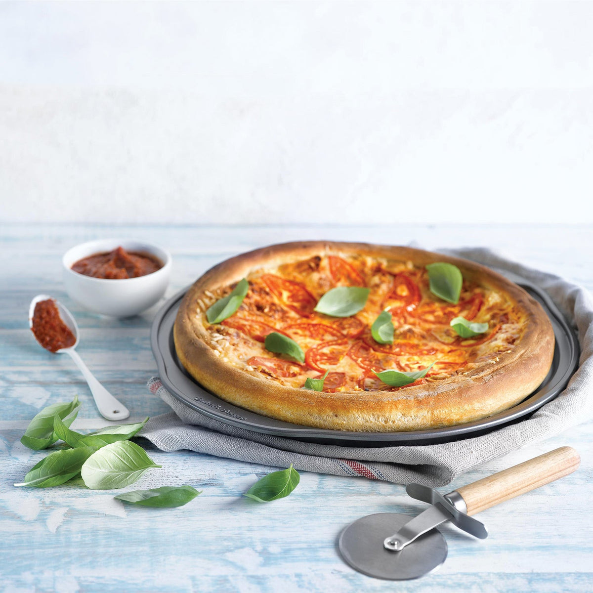 Homemade pizza on a pizza crisper with a pizza cutter