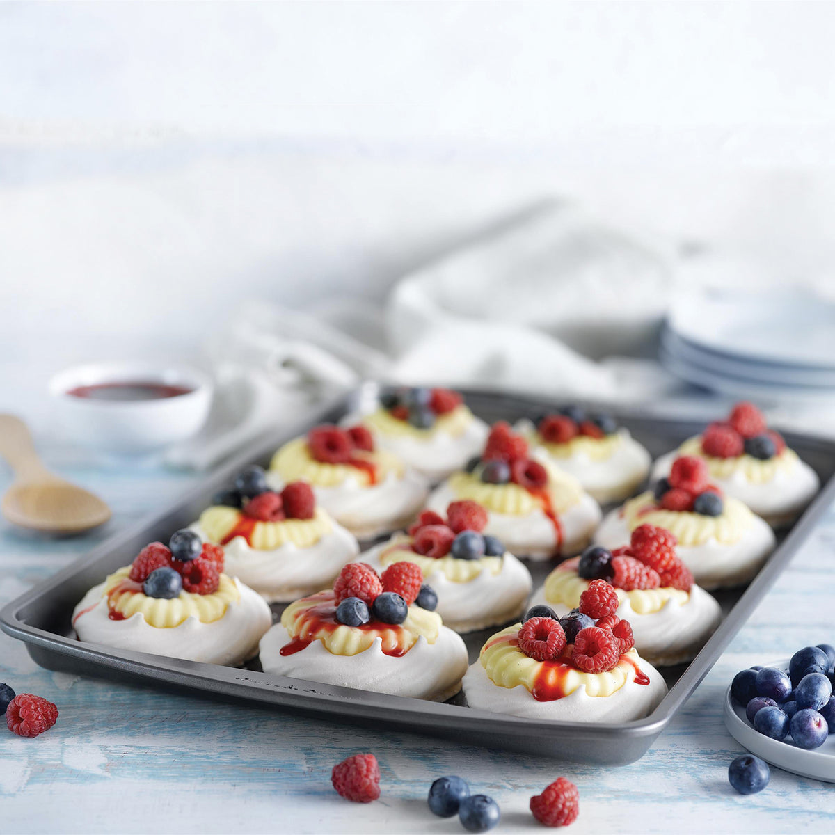 Cream-topped pastries with fresh berries on a baking pan